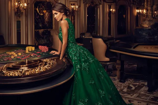 A woman in a luxurious green gown next to an ornate roulette wheel, capturing the upscale casino mood of SPINARA.